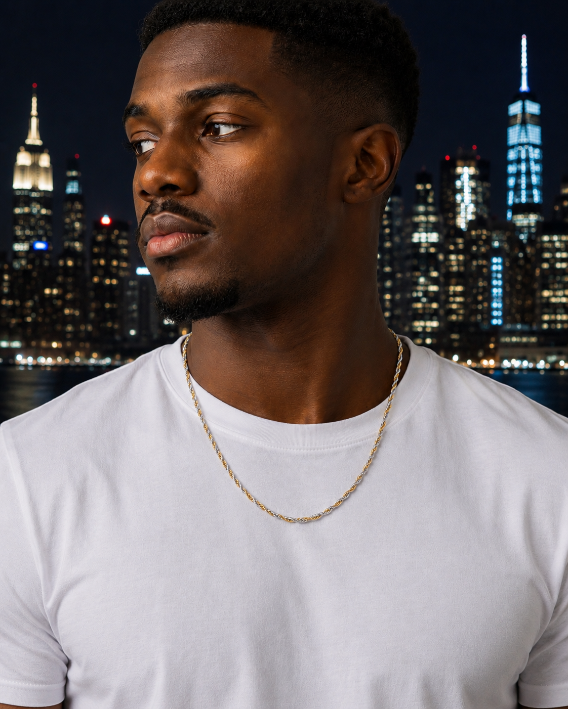 Man wearing a white t-shirt with a gold chain, standing against a city skyline at night.