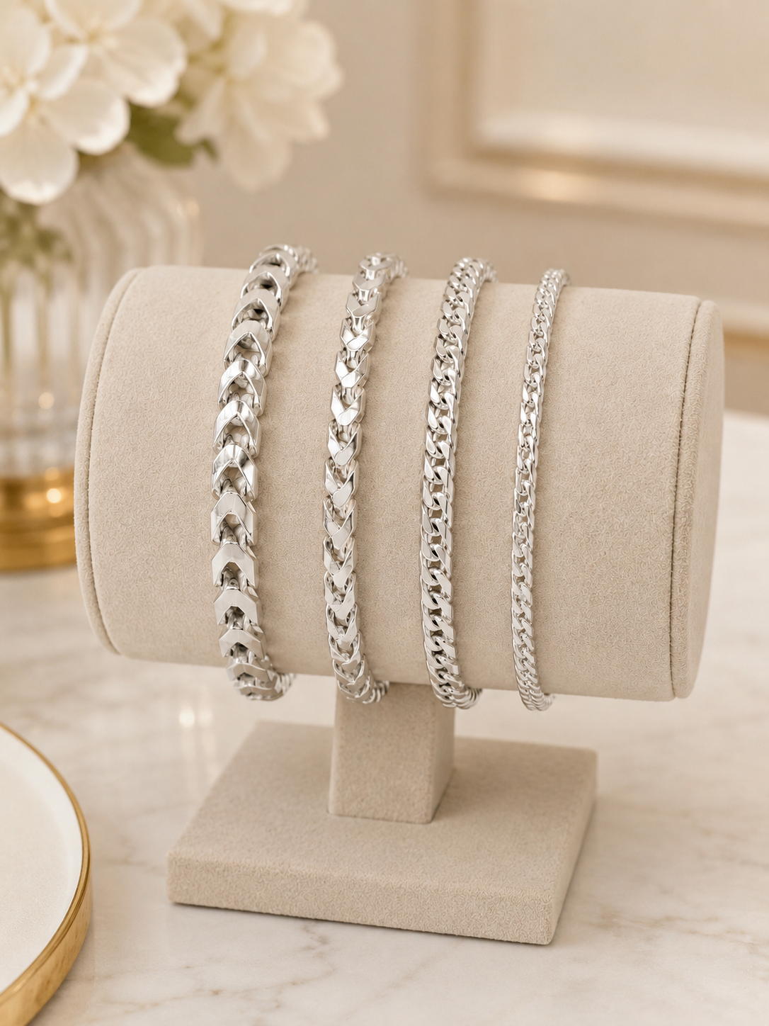 Set of silver chain bracelets on a beige jewelry stand with a blurred floral background
